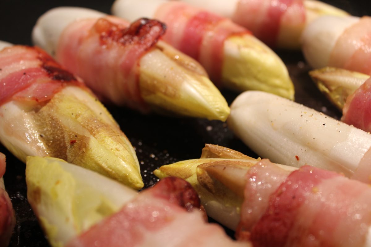 Chicons poêlés enroulés de lard dans une poêle
